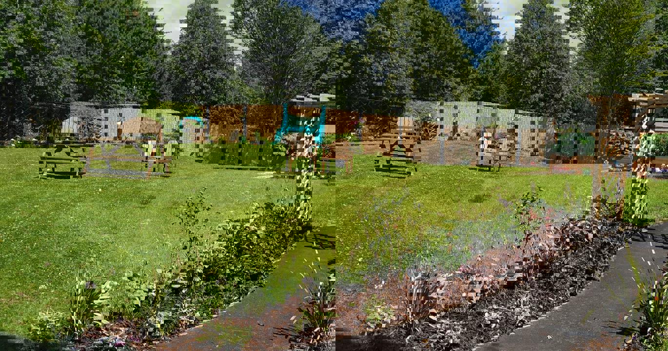 A lovely green garden with wooden furniture in the background, a curved tarmac walkway bordered by flower beds in the foreground