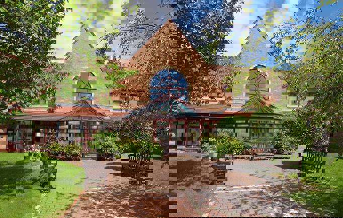 The entrance to Swan Court, a welcoming building with two wooden benches and a wide accessible walkway borderd by lush green lawns