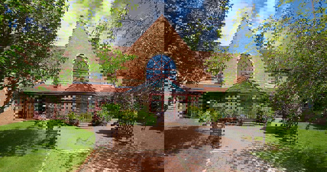 The entrance to Swan Court, a welcoming building with two wooden benches and a wide accessible walkway borderd by lush green lawns