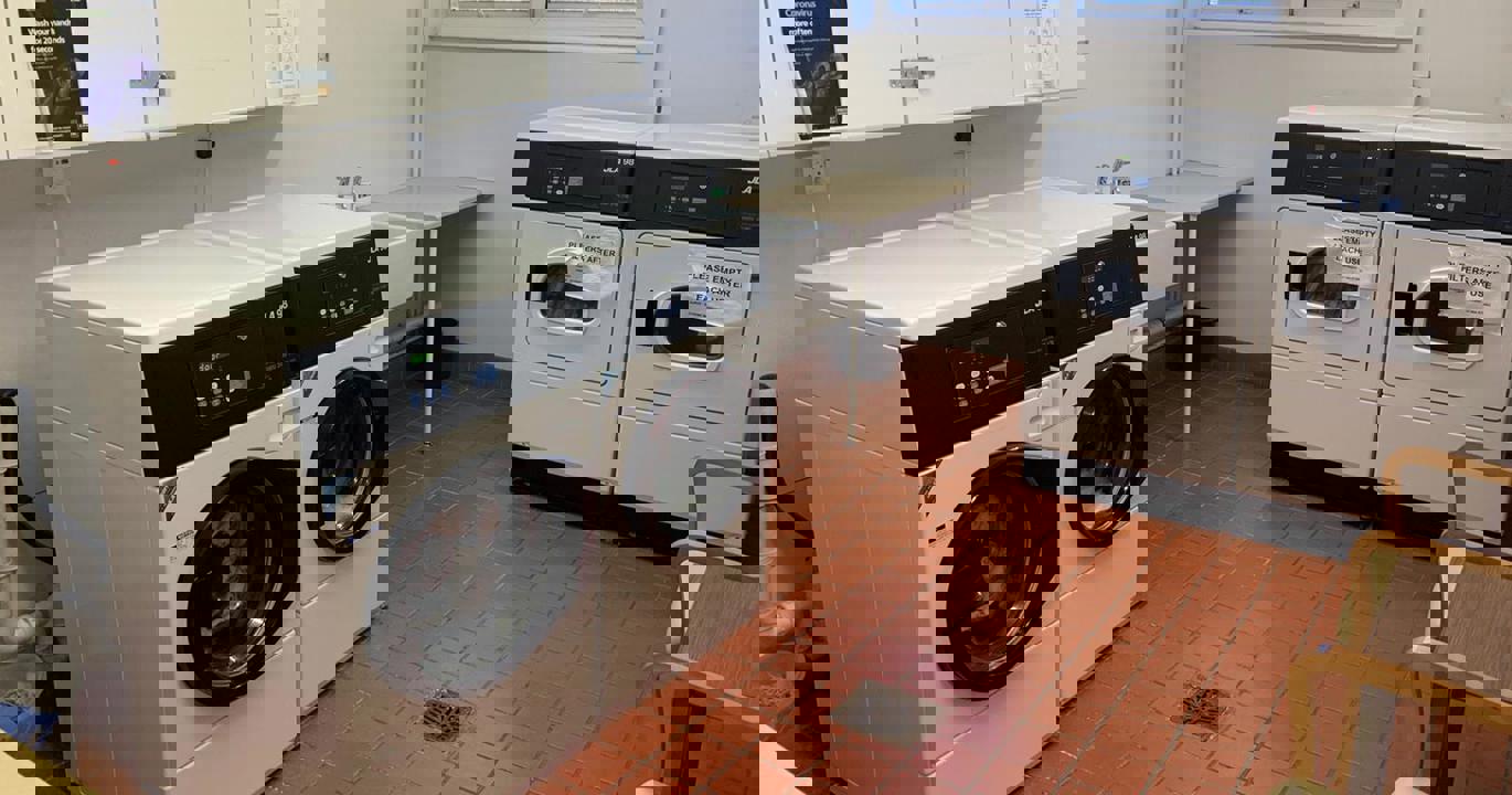 A laundry room with two large washing machines, two tumble driers and a sink