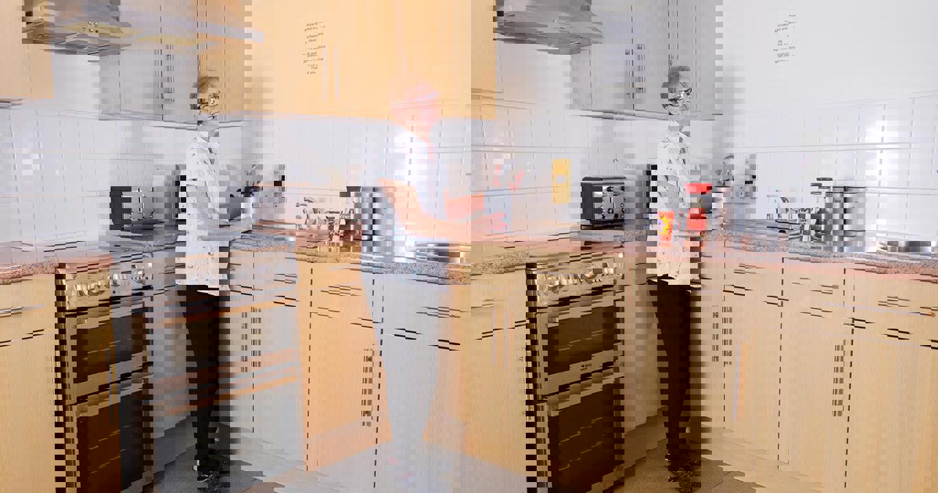 A smiling woman opens a coffee jar in a kitchen with an oven, sink, toaster and other amenities